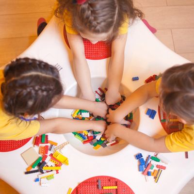 Three children playing with colorful building blocks around a circular table.