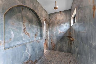 Arched stone shower with decorative wall tile, bench seating and brass fixtures