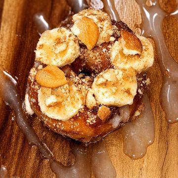 Donut topped with banana slices, nuts, and drizzle on wooden surface.