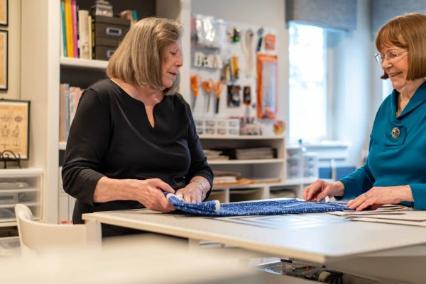 Two women working on fabric at a crafting table.