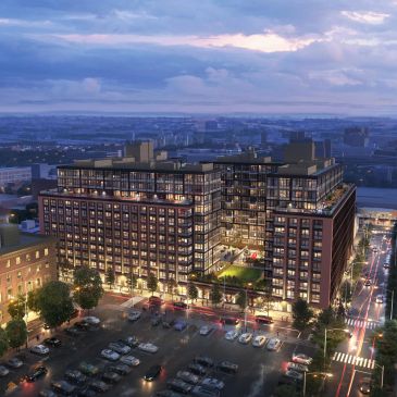 Large modern apartment complex illuminated at dusk in a city.