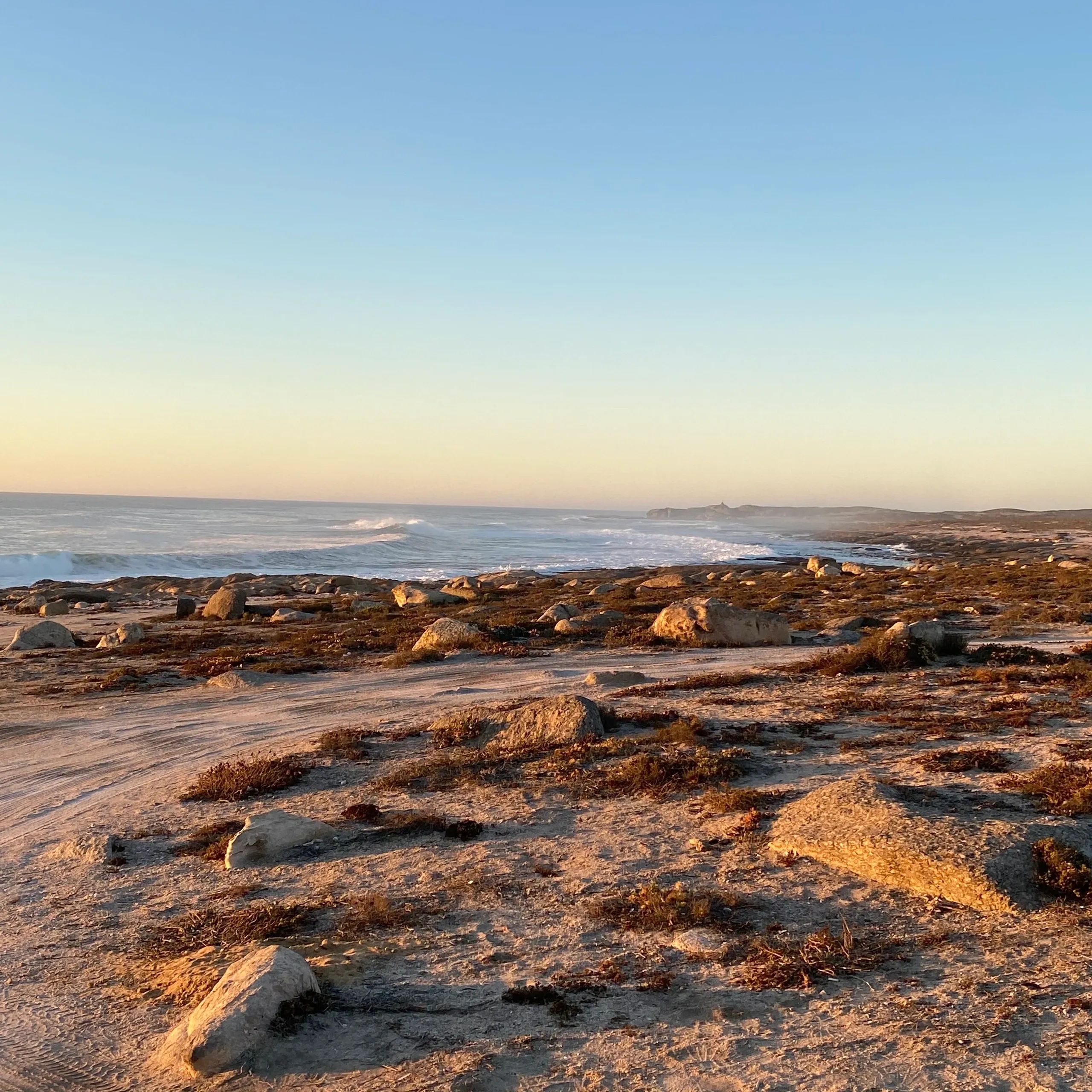 Rocky shoreline with waves under a clear sky at sunset.