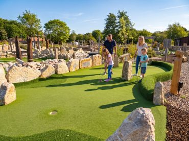 Family playing mini golf outdoors in sunny weather. Stonebridge Adventure Golf course near Birmingham West Midlands