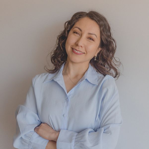 Mujer sonriente con camisa azul claro y cabello rizado.
