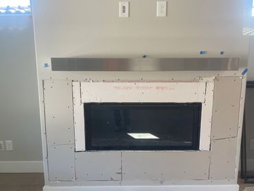 Unfinished fireplace installation with drywall patches and a metal mantel.