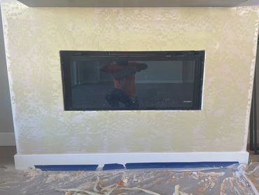 Fireplace installation in progress with textured wall and protective floor covering.