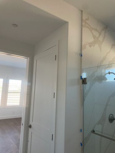 White door next to a shower with marble-patterned walls and blue painter's tape.