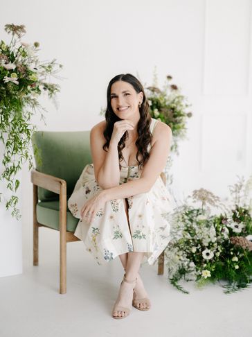 Woman in floral dress sitting on green chair and smiling.