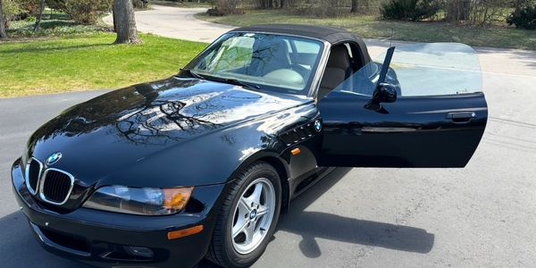 Black BMW convertible with open driver door parked on driveway.