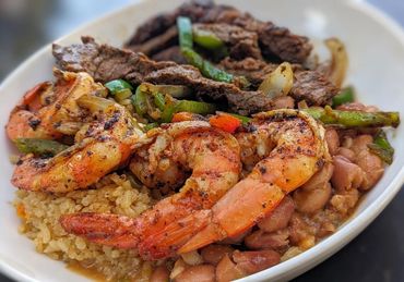 Grilled shrimp and steak with rice, beans, and veggies in a bowl.