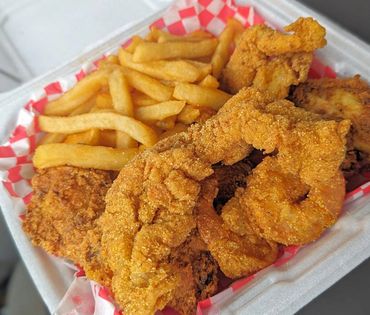 A takeout box with fried shrimp, fried chicken, and French fries.