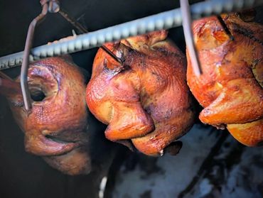 Three whole chickens being smoked on metal hooks in a smoker.