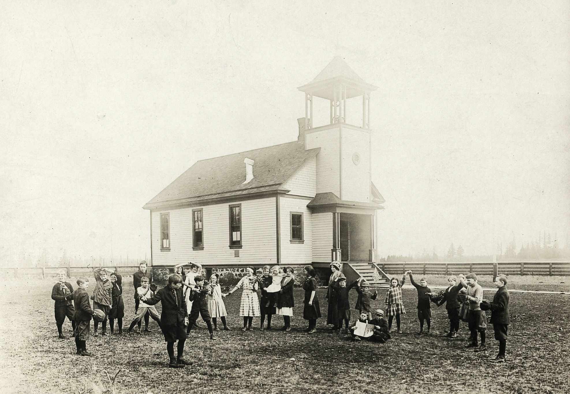 Black and white photo of a group of children posed outside a one-room schoolhouse with a bell tower.