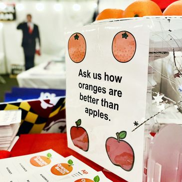 Sign promoting oranges over apples at a display stall.