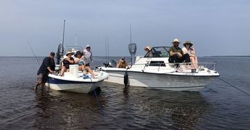 Two boats with people enjoying a calm fishing day on the water under a clear sky.