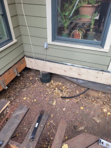 House exterior showing foundation repair with new wooden siding and exposed ground.