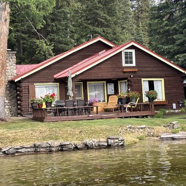 Cozy lakeside cabin with a wooden deck and flower pots.