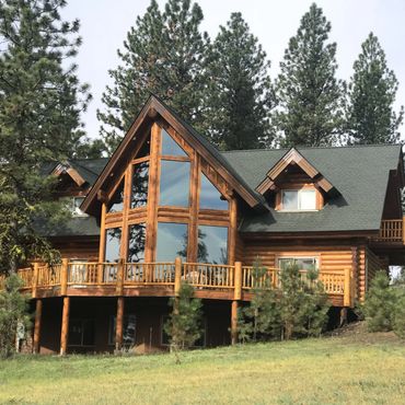 A large wooden log cabin with big glass windows surrounded by pine trees.