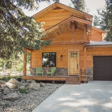 Rustic wooden house with a stone-accented porch and green chairs.