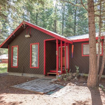 Cozy brown cabin with red trim nestled in a forested area.