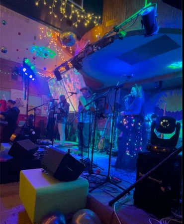 Live band performing on a colorful, festive stage with vibrant lighting and decorations.