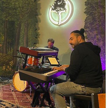 Two musicians playing keyboard and drums in a cozy indoor setting.