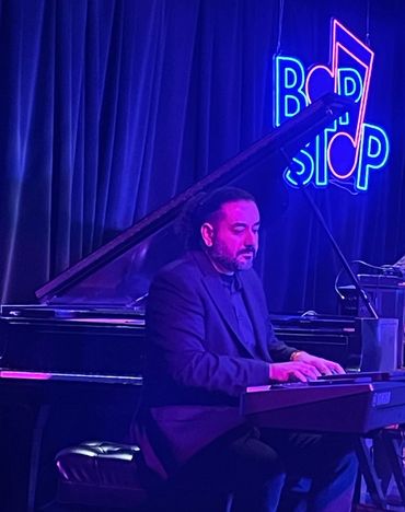 A man playing a keyboard in a dimly lit music venue with a neon sign.