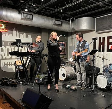 Band performing live on stage with keyboard, vocals, guitar, and drums.