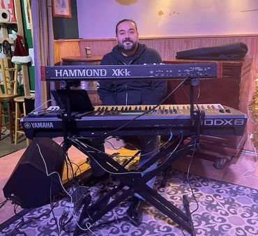 Man sitting behind two keyboards on a stand in a cozy room.