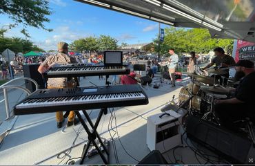 Band performing live on an outdoor stage with keyboards and drums.