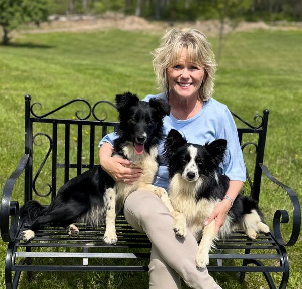 Woman sitting on a bench with two black and white dogs.