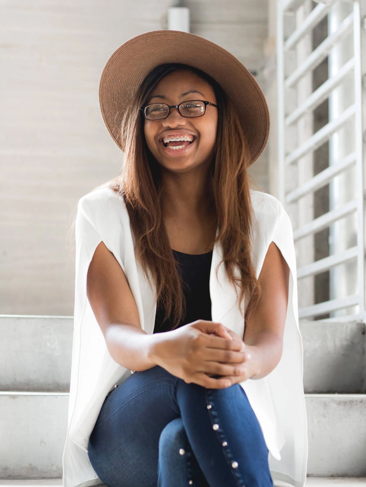Smiling woman with glasses and a wide-brimmed hat sitting on stairs.