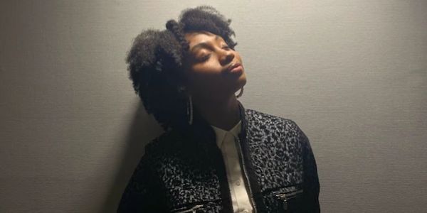 Woman with natural hair enjoying sunlight against a plain wall.