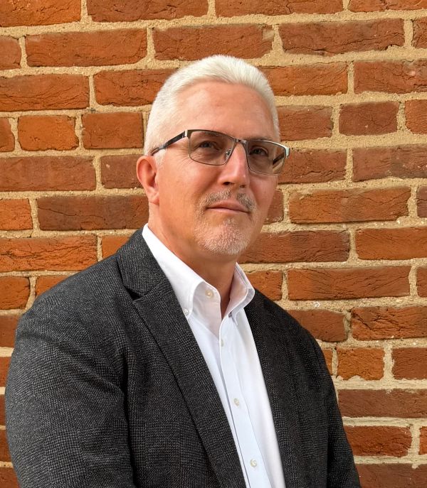 Confident man with glasses and gray hair in front of a brick wall.