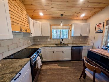 Cozy kitchen with wooden ceiling, white cabinets, and granite countertops.