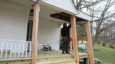 Man working on porch roof repairs with wooden beams and tools.