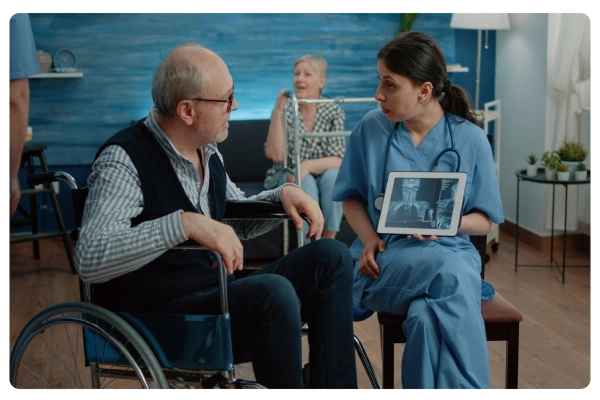 Nurse showing X-ray to elderly man in wheelchair during consultation.