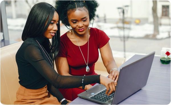 Two women collaborating and smiling while using a laptop indoors.