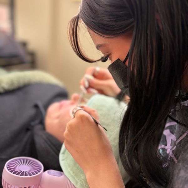 A person wearing a mask carefully applying eyelash extensions to a client.