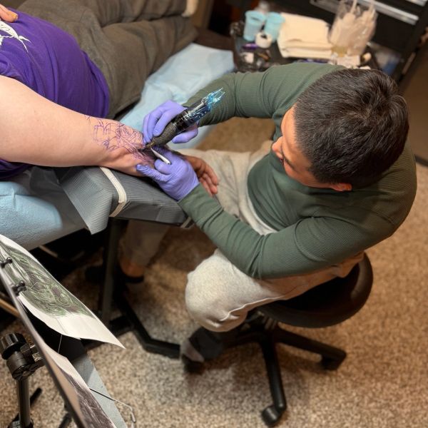 A tattoo artist is working on a client's hand tattoo.
