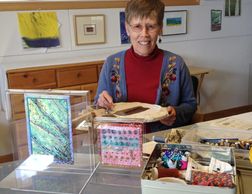 Katherine Colwell working in her studio with 2-sided and framed embroidery for sale.