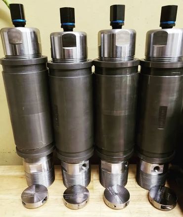 Four large metal mechanical components with threaded ends.