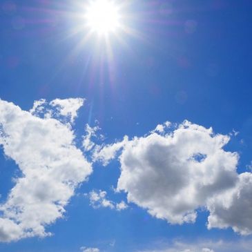 Bright sun shining in a clear blue sky with fluffy white clouds.