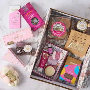 A curated gift box with chocolates, bath salts, candle, and skincare items.