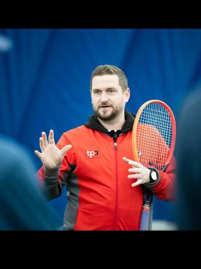 Man in red jacket holding tennis racket, explaining something.