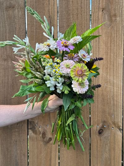 Hand holding a colorful wildflower bouquet against a wooden fence.