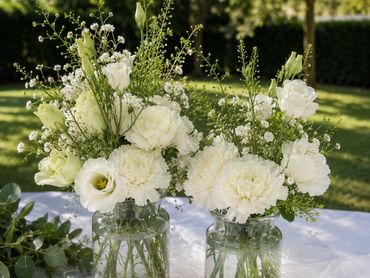 Two jars with white flowers and a candle on a table outdoors.