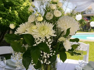 Elegant white flower bouquet in a glass vase at an outdoor event.