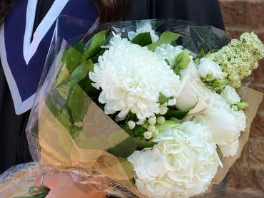 Person in graduation gown holding a bouquet of white flowers.