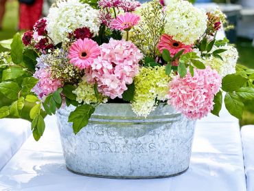 Colorful flower arrangement in a metal bucket on a table.